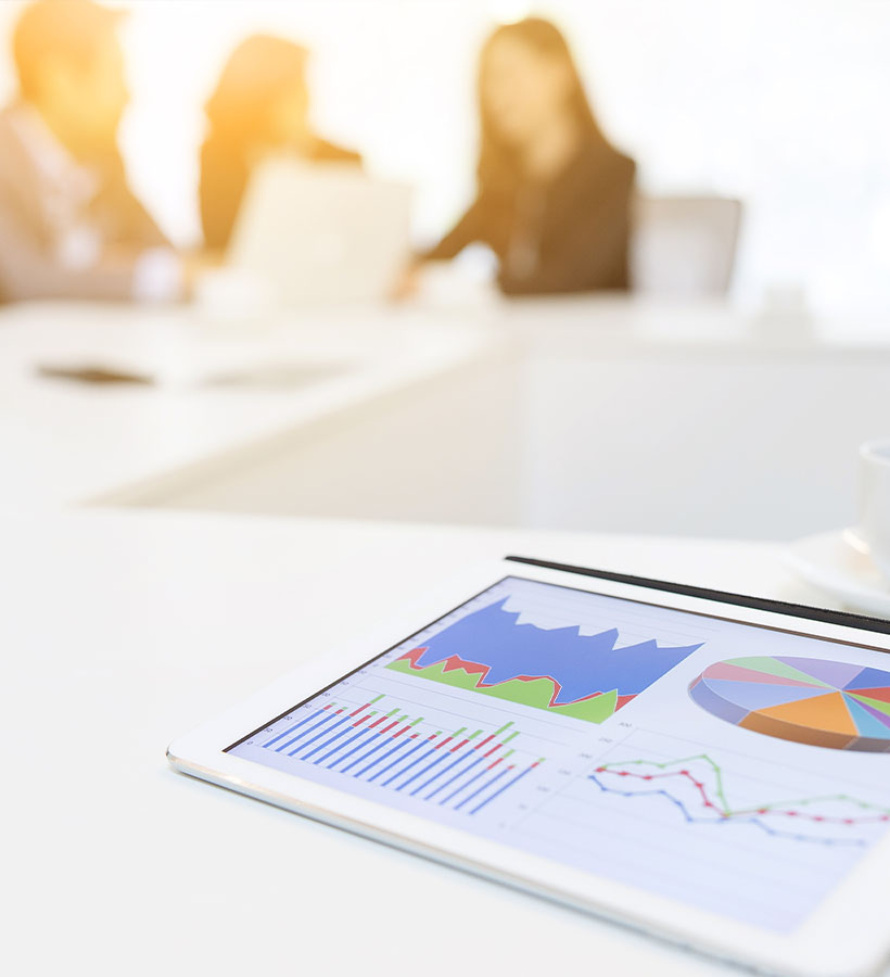 Una tablet muestra gráficos y se ven unos empleados de fondo